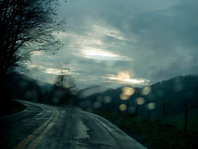 A wet road curving under a grey sky, seen through a windshield
