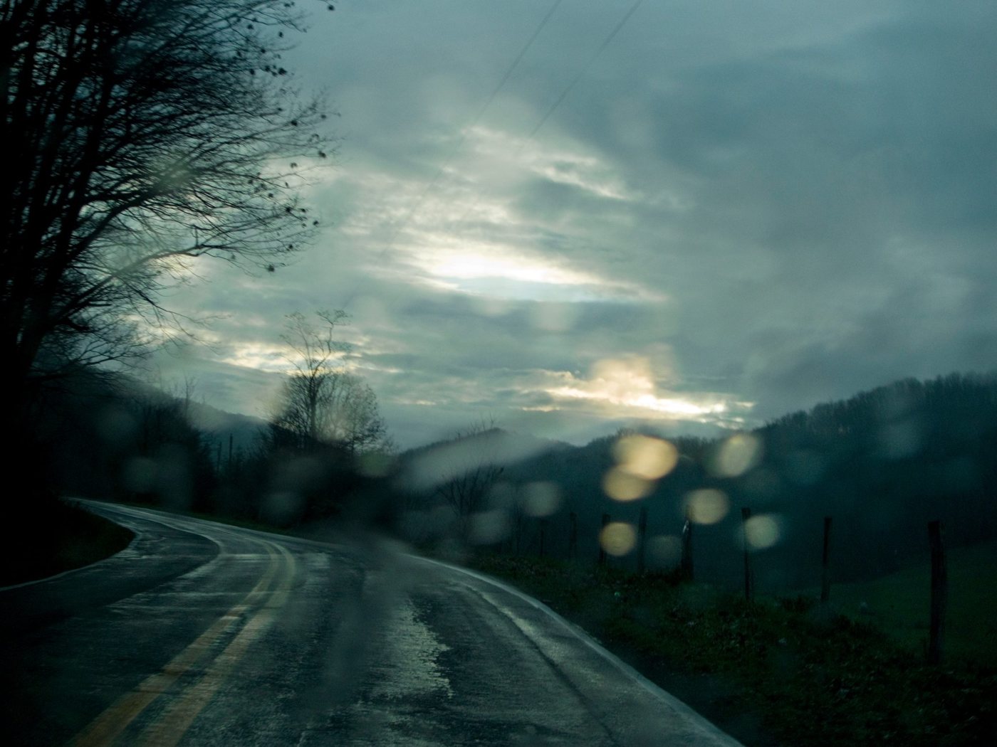 A wet road curving under a grey sky, seen through a windshield