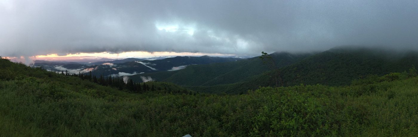 Storm clouds over dark forested ridges at first light, mist lying in the valleys